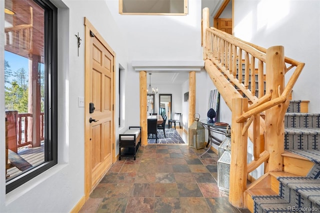 foyer entrance featuring baseboards, stone finish flooring, stairway, and an inviting chandelier