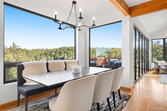 dining room with a wealth of natural light, wood finished floors, a view of trees, and an inviting chandelier