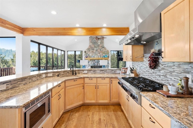 kitchen with appliances with stainless steel finishes, light stone counters, island exhaust hood, light brown cabinets, and a sink