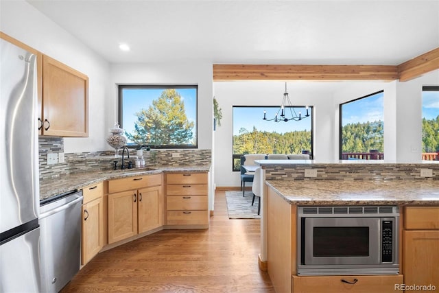 kitchen with light brown cabinetry, appliances with stainless steel finishes, a sink, and tasteful backsplash