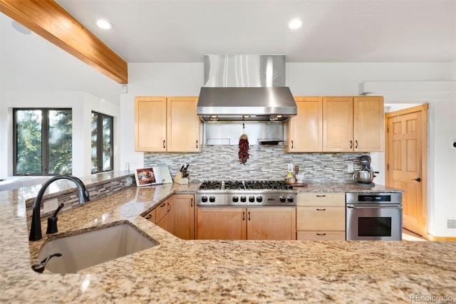 kitchen with decorative backsplash, wall chimney exhaust hood, appliances with stainless steel finishes, light brown cabinets, and a sink