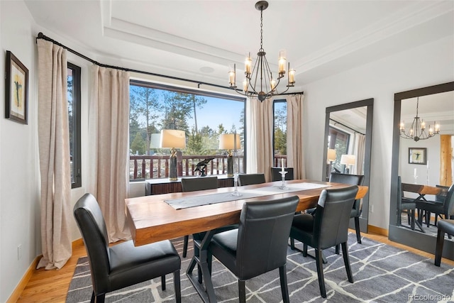 dining space with an inviting chandelier, baseboards, a raised ceiling, and wood finished floors