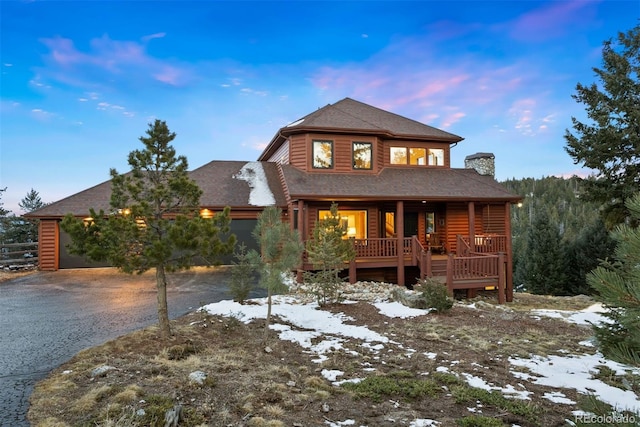 view of front of property with aphalt driveway, covered porch, a garage, faux log siding, and a chimney