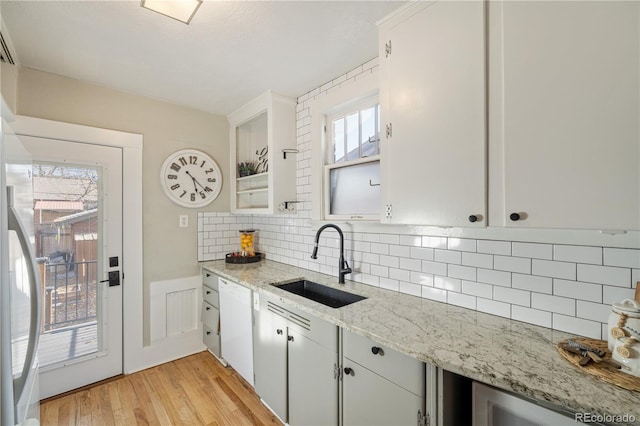 kitchen with white dishwasher, sink, light wood-type flooring, light stone counters, and white cabinetry