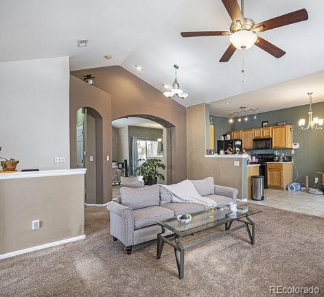 living area featuring arched walkways, light carpet, ceiling fan with notable chandelier, baseboards, and vaulted ceiling