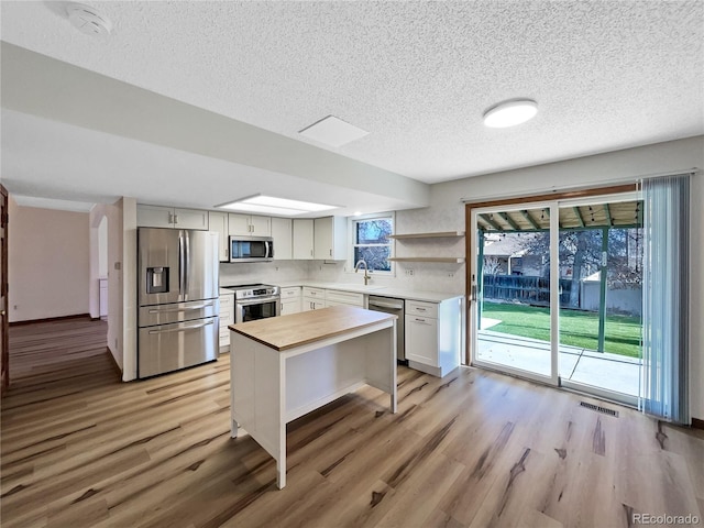 kitchen featuring white cabinets, sink, light hardwood / wood-style flooring, a textured ceiling, and appliances with stainless steel finishes