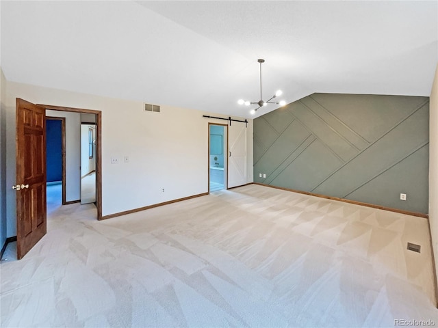 empty room featuring a chandelier, a barn door, light colored carpet, and vaulted ceiling