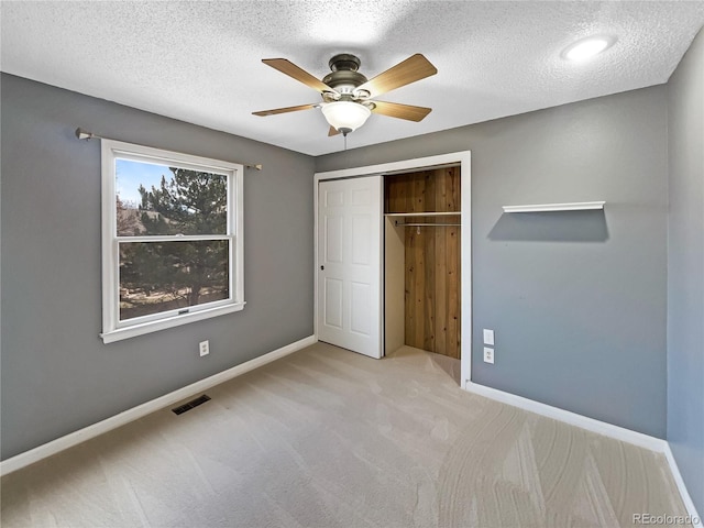 unfurnished bedroom with light carpet, a textured ceiling, a closet, and ceiling fan