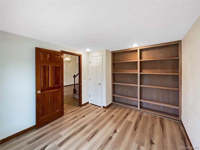 unfurnished bedroom featuring light hardwood / wood-style floors, a textured ceiling, and a chandelier