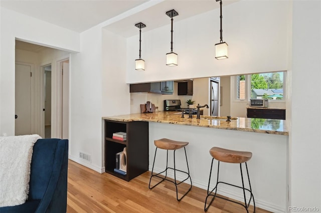 1370 S Hudson St, Denver, CO 80222 - kitchen with appliances with stainless steel finishes, a kitchen breakfast bar, light wood-type flooring, hanging light fixtures, and light stone counters