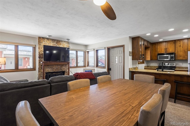 dining space featuring a ceiling fan, a stone fireplace, recessed lighting, and plenty of natural light