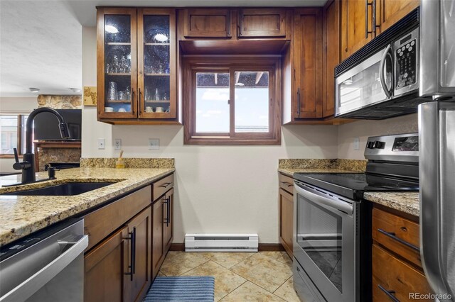 kitchen with glass insert cabinets, a baseboard heating unit, baseboards, a sink, and appliances with stainless steel finishes
