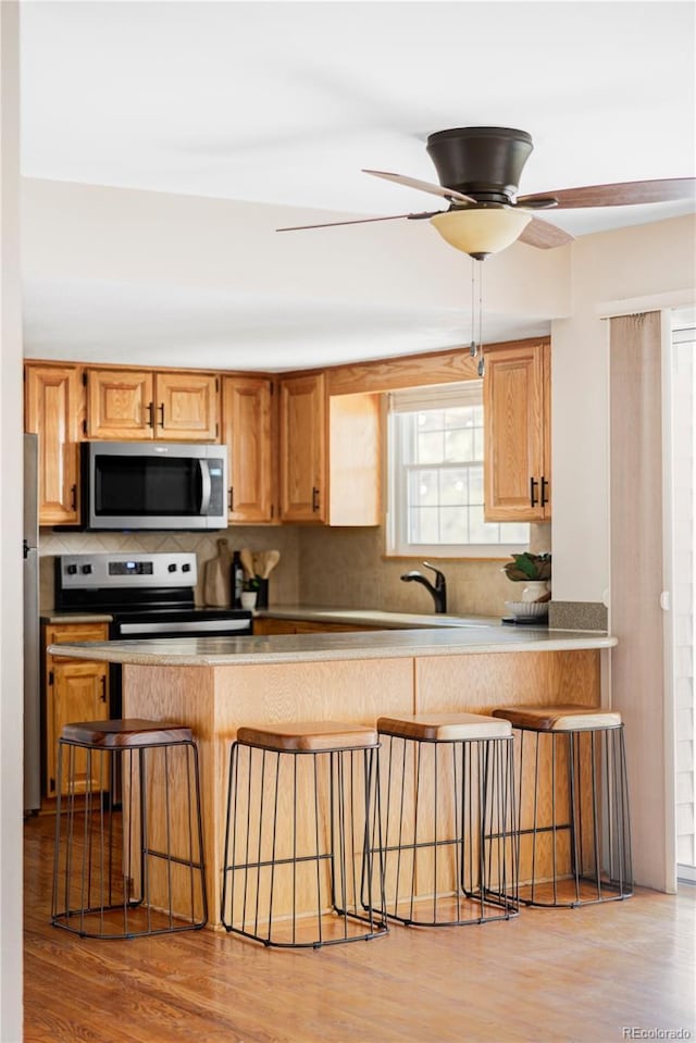 kitchen featuring light wood-type flooring, stainless steel appliances, a kitchen breakfast bar, and decorative backsplash