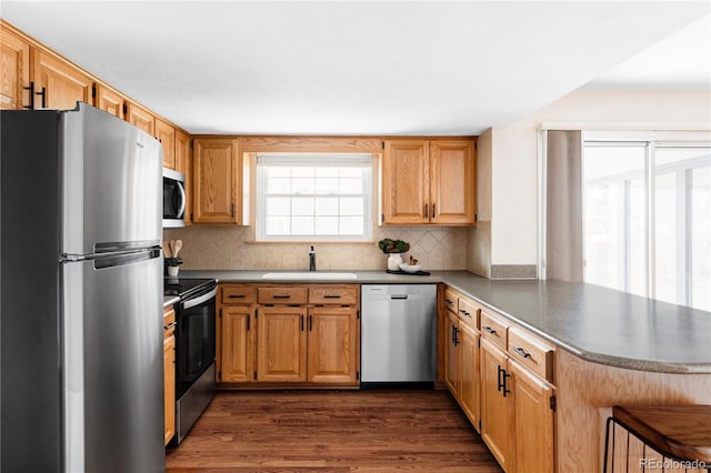 kitchen with tasteful backsplash, dark wood finished floors, appliances with stainless steel finishes, a peninsula, and a sink