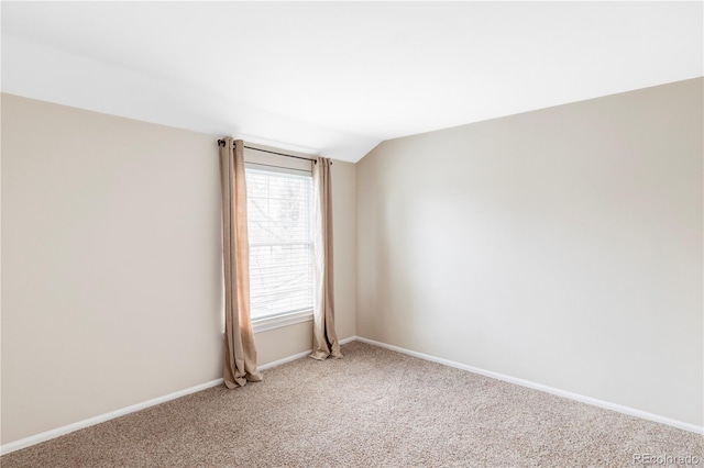 spare room with baseboards, lofted ceiling, and light carpet