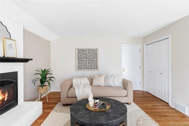 living room with visible vents, lofted ceiling, wood finished floors, baseboards, and a brick fireplace