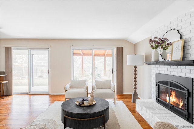 living area with a brick fireplace, baseboards, lofted ceiling, and wood finished floors