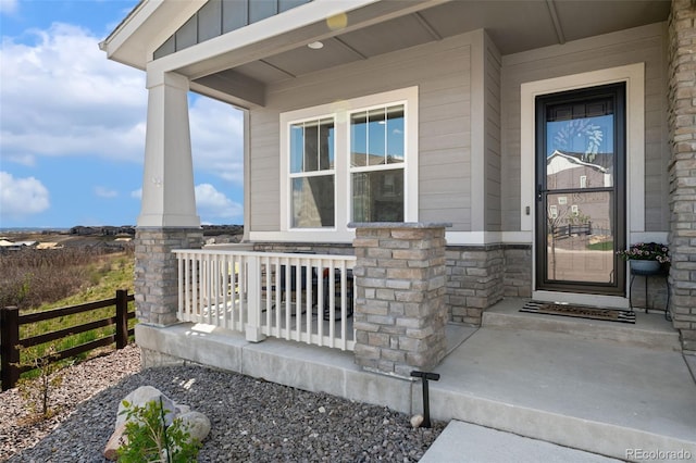 doorway to property featuring a porch, board and batten siding, fence, and stone siding