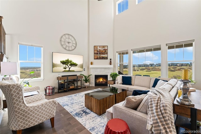 living room with a warm lit fireplace, a high ceiling, and dark wood-style floors