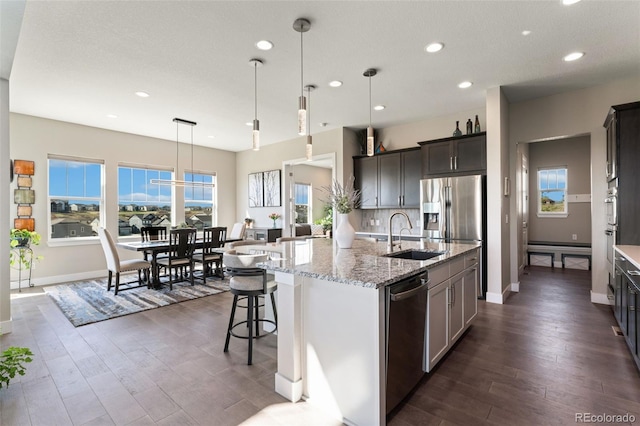 kitchen featuring light stone counters, appliances with stainless steel finishes, a sink, dark wood finished floors, and recessed lighting