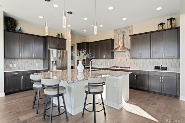 kitchen featuring a sink, wood finished floors, wall chimney range hood, and stainless steel appliances