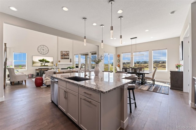 kitchen with dark wood-style flooring, stainless steel dishwasher, a sink, light stone counters, and recessed lighting