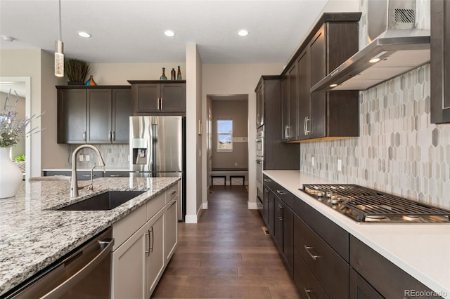 kitchen featuring dark brown cabinetry, dark wood-style floors, wall chimney exhaust hood, a sink, and appliances with stainless steel finishes
