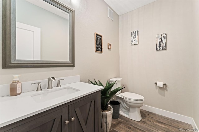 half bath featuring visible vents, wood finished floors, baseboards, vanity, and toilet