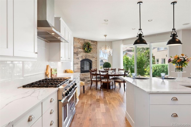 4142 Saltbrush Ct, Loveland, CO 80538 - kitchen featuring wall chimney exhaust hood, high end range, light wood-style flooring, tasteful backsplash, and white cabinets