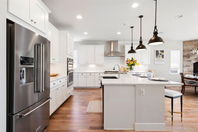 4142 Saltbrush Ct, Loveland, CO 80538 - kitchen with appliances with stainless steel finishes, wall chimney range hood, white cabinetry, a kitchen breakfast bar, and recessed lighting