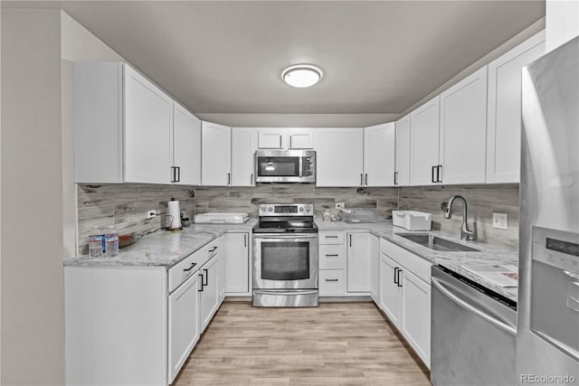 kitchen with white cabinetry, sink, stainless steel appliances, light stone counters, and light hardwood / wood-style flooring