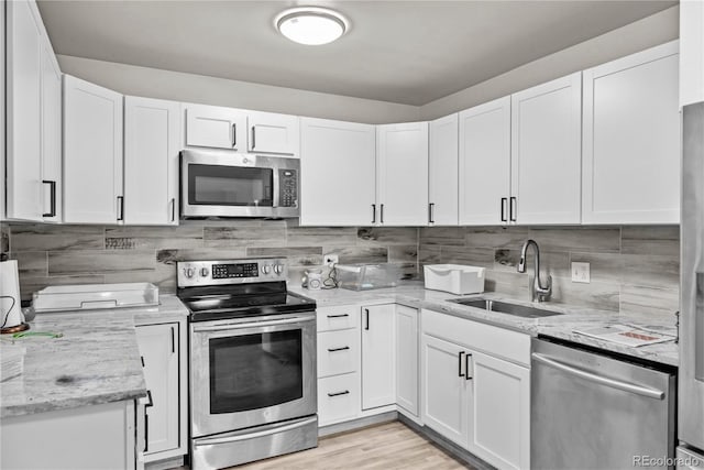 kitchen with sink, light hardwood / wood-style flooring, appliances with stainless steel finishes, light stone counters, and white cabinetry