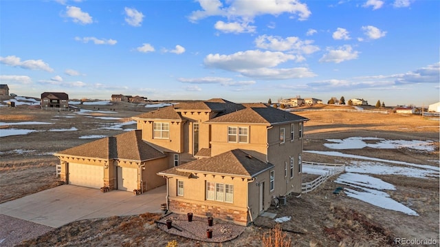 view of front of home featuring an attached garage, central AC, a shingled roof, stucco siding, and concrete driveway