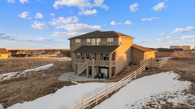 snow covered rear of property with stucco siding, stairs, and fence