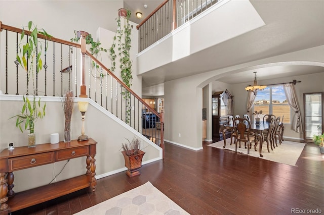 foyer entrance featuring baseboards, stairway, hardwood / wood-style floors, an inviting chandelier, and arched walkways