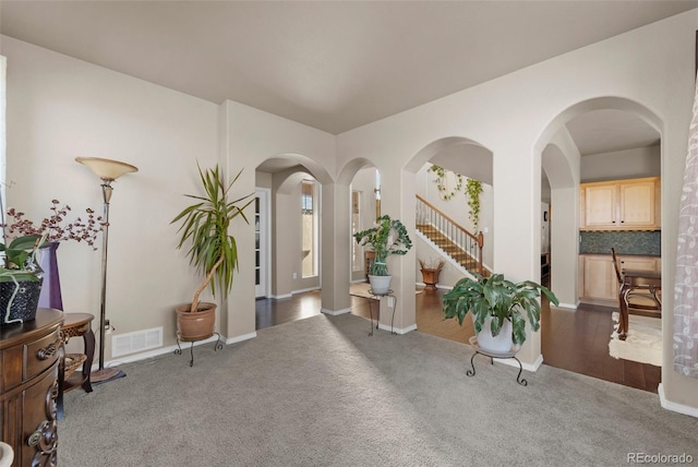 carpeted foyer entrance featuring stairway, arched walkways, and visible vents