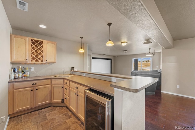 kitchen with light brown cabinets, wine cooler, open floor plan, a peninsula, and a sink