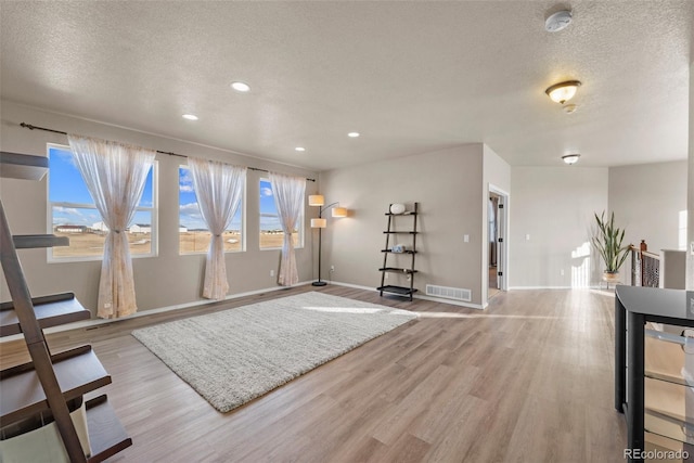 living area with visible vents, a textured ceiling, recessed lighting, light wood finished floors, and baseboards