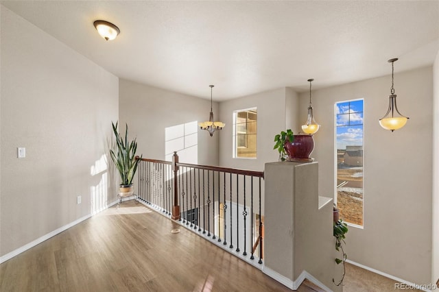 corridor with an upstairs landing, an inviting chandelier, baseboards, and wood finished floors