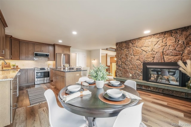 dining room featuring sink, a stone fireplace, and light hardwood / wood-style floors