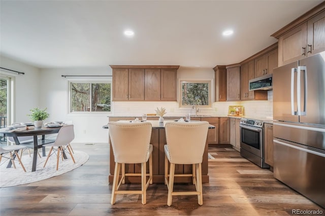 kitchen featuring tasteful backsplash, appliances with stainless steel finishes, a kitchen bar, and dark wood-type flooring