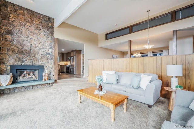 living room with beamed ceiling, a stone fireplace, a chandelier, and light carpet