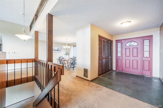 entryway with an inviting chandelier, a textured ceiling, and dark colored carpet