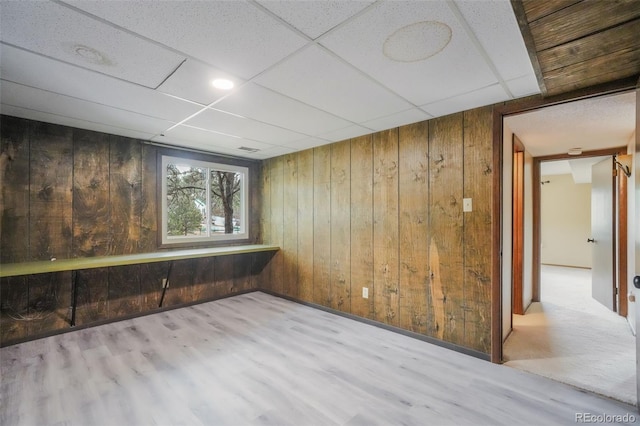 empty room featuring wooden walls, light hardwood / wood-style floors, and a paneled ceiling