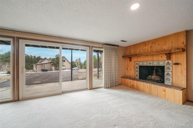 unfurnished living room featuring wooden walls, a tile fireplace, carpet, and a textured ceiling