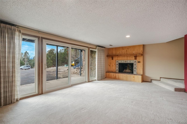 unfurnished living room with a tile fireplace, light colored carpet, and a textured ceiling