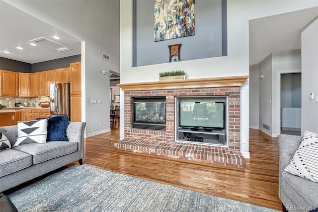 581 Stonemont Dr, Castle Pines, CO 80108 - living area with attic access, wood finished floors, a brick fireplace, baseboards, and a towering ceiling