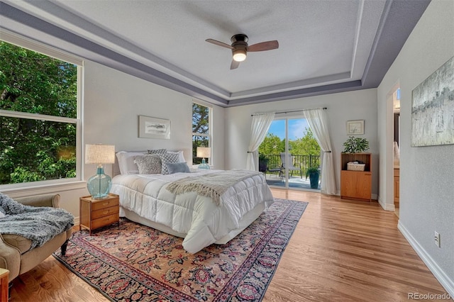 581 Stonemont Dr, Castle Pines, CO 80108 - bedroom featuring a tray ceiling, access to exterior, light wood-style floors, a ceiling fan, and baseboards