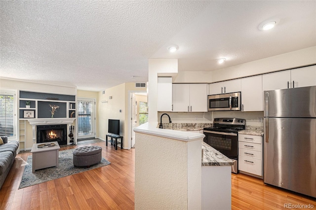 2 Acoma St Unit 11, Denver, CO 80223 - kitchen featuring appliances with stainless steel finishes, a textured ceiling, light wood-type flooring, white cabinets, and plenty of natural light