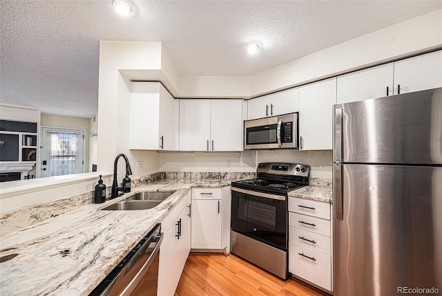 2 Acoma St Unit 11, Denver, CO 80223 - kitchen with appliances with stainless steel finishes, a sink, a textured ceiling, light wood-style flooring, and white cabinets